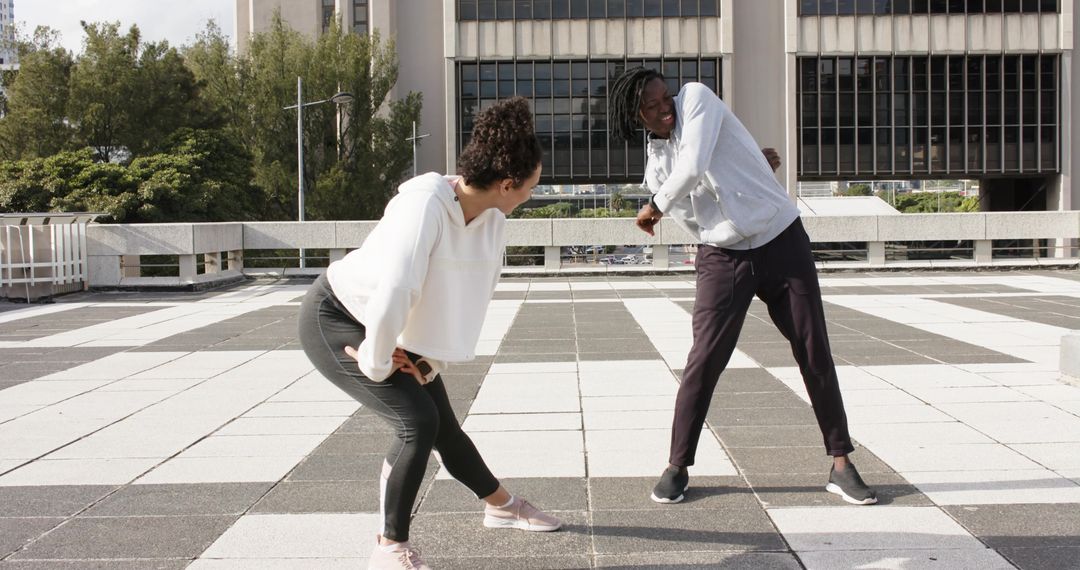 Diverse pair stretching on urban rooftop with checkered tile floor wearing workout gear