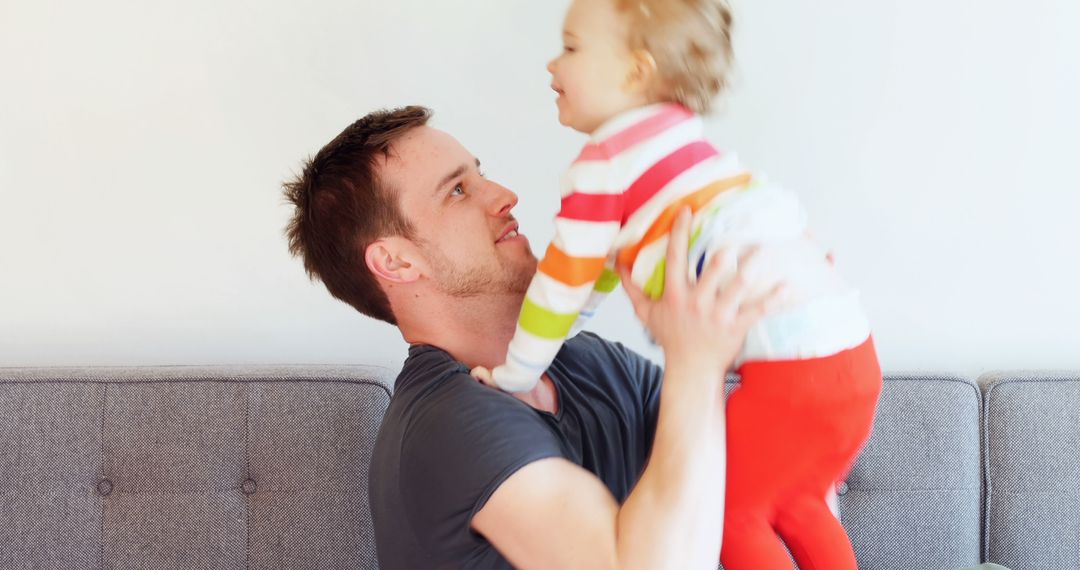 Father lifting smiling toddler on sofa indoors - Free Images, Stock Photos and Pictures on Pikwizard.com