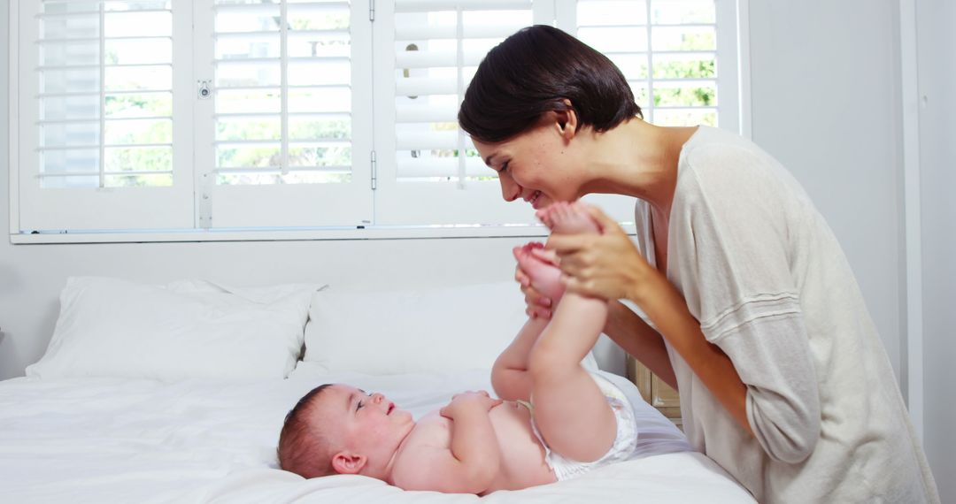 Mother Smiling and Playing with Baby on Bed in Bright Bedroom - Free Images, Stock Photos and Pictures on Pikwizard.com