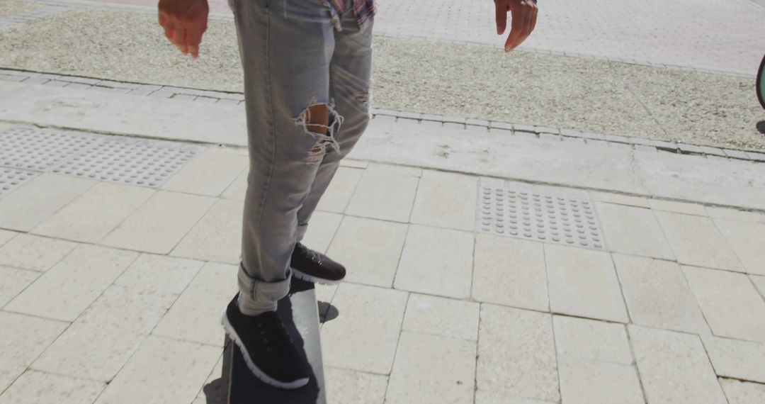 Male Skateboarder Balancing on Tiled Sidewalk in Ripped Jeans