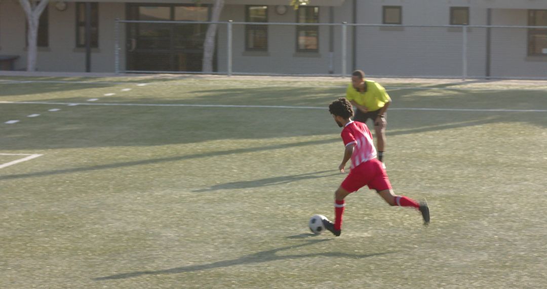Soccer Player in Motion with Referee Observing on Grass Field