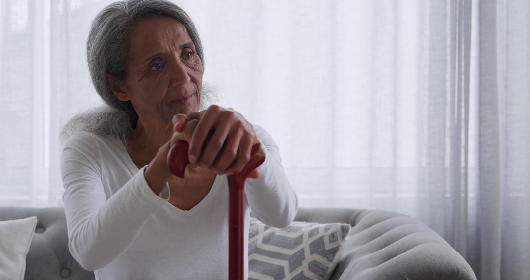 Elderly Woman Sitting on Couch Holding Cane Thoughtfully - Free Images, Stock Photos and Pictures on Pikwizard.com