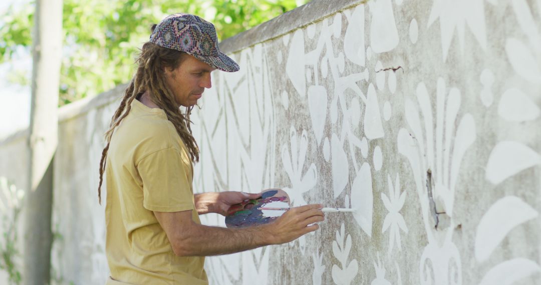 Image of happy caucasian male artist with dreadlocks painting mural on wall - Free Images, Stock Photos and Pictures on Pikwizard.com