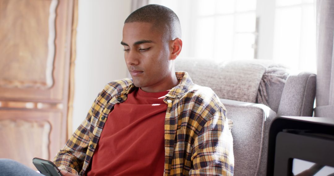 Young Man Sitting Relaxing on Sofa Using Smartphone at Home - Free Images, Stock Photos and Pictures on Pikwizard.com