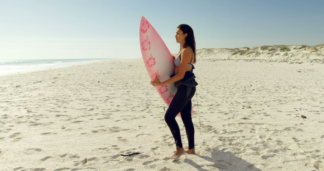 Woman holding pink surfboard on sandy beach during sunny day - Free Images, Stock Photos and Pictures on Pikwizard.com