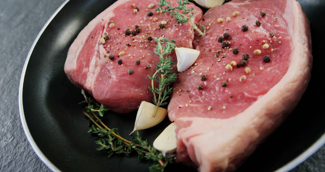 Raw Steaks with Garlic, Peppercorns, and Fresh Herbs on Black Plate - Free Images, Stock Photos and Pictures on Pikwizard.com