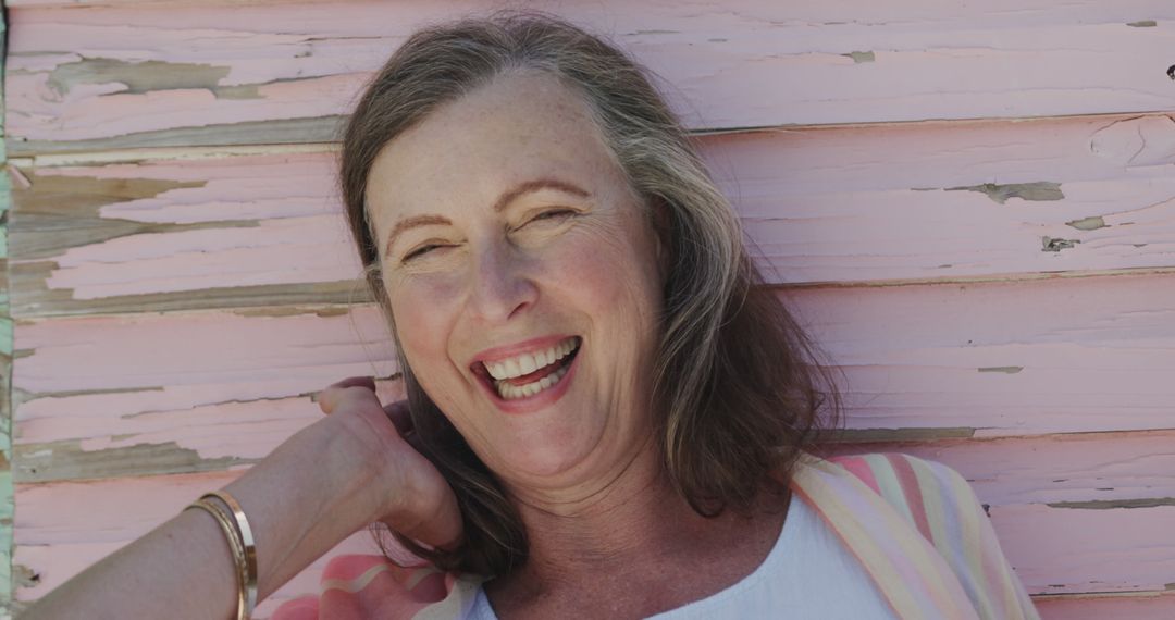 Laughing Mature Woman Posing Against Weathered Pink Wall - Free Images, Stock Photos and Pictures on Pikwizard.com