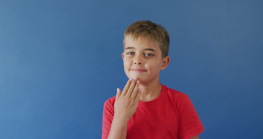 Smiling Boy in Red Shirt Touching Chin Against Blue Background - Free Images, Stock Photos and Pictures on Pikwizard.com