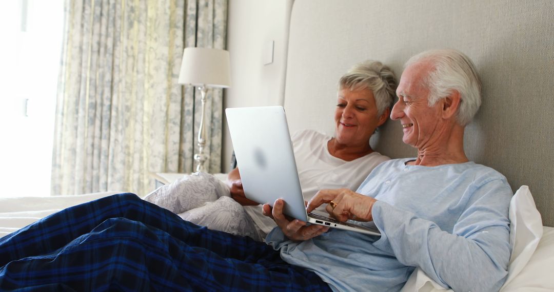 Senior Couple Relaxing on Bed Using Laptop in Light Bedroom