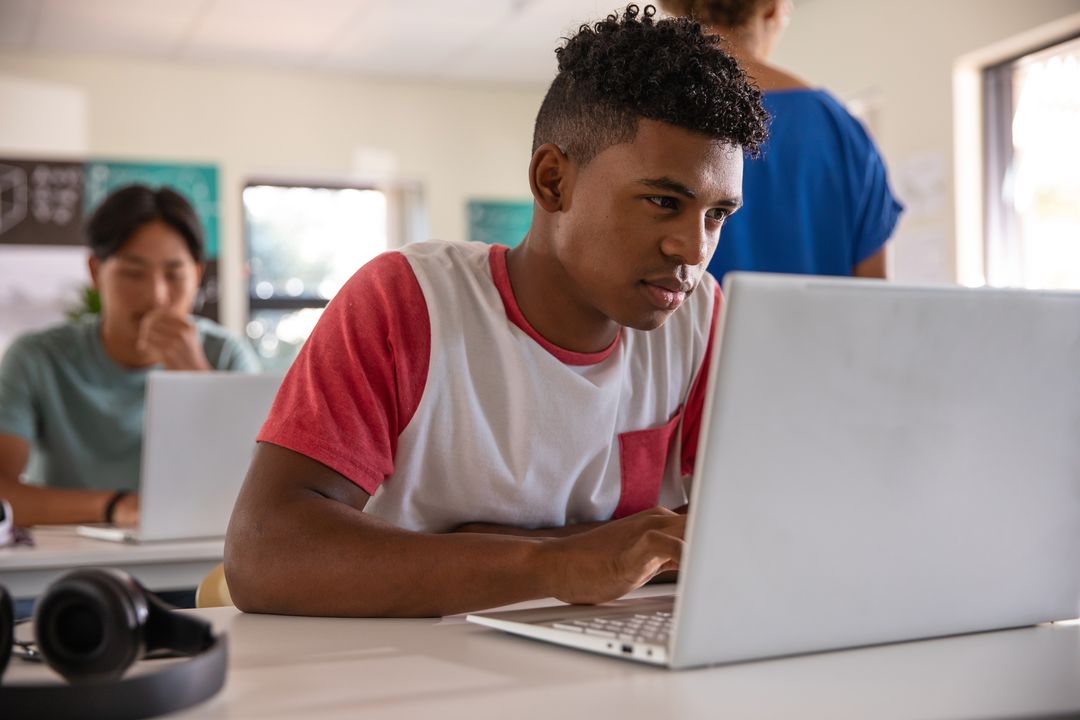Focused Multiracial Teens Typing on Laptops in Classroom Collaborating on School Projects