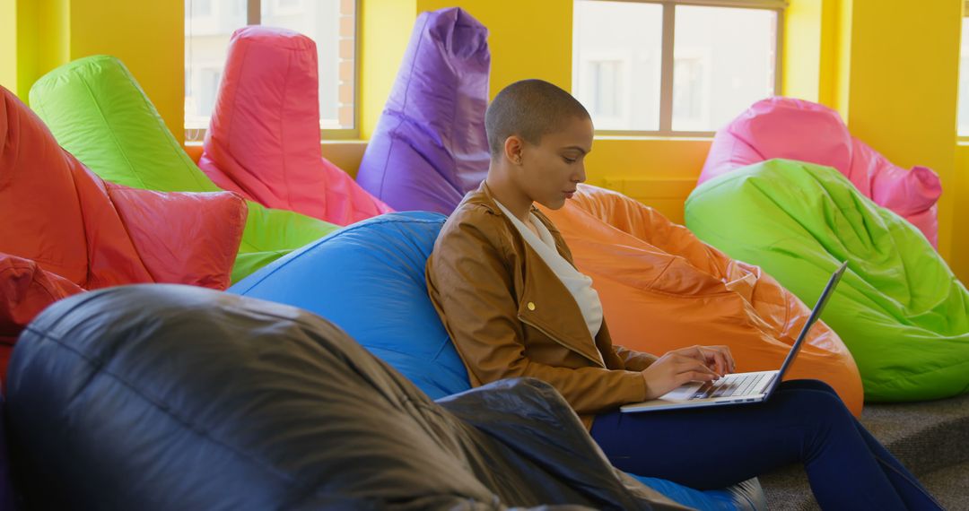 Young Woman Working on Laptop in Colorful Bean Bag Lounge - Free Images, Stock Photos and Pictures on Pikwizard.com