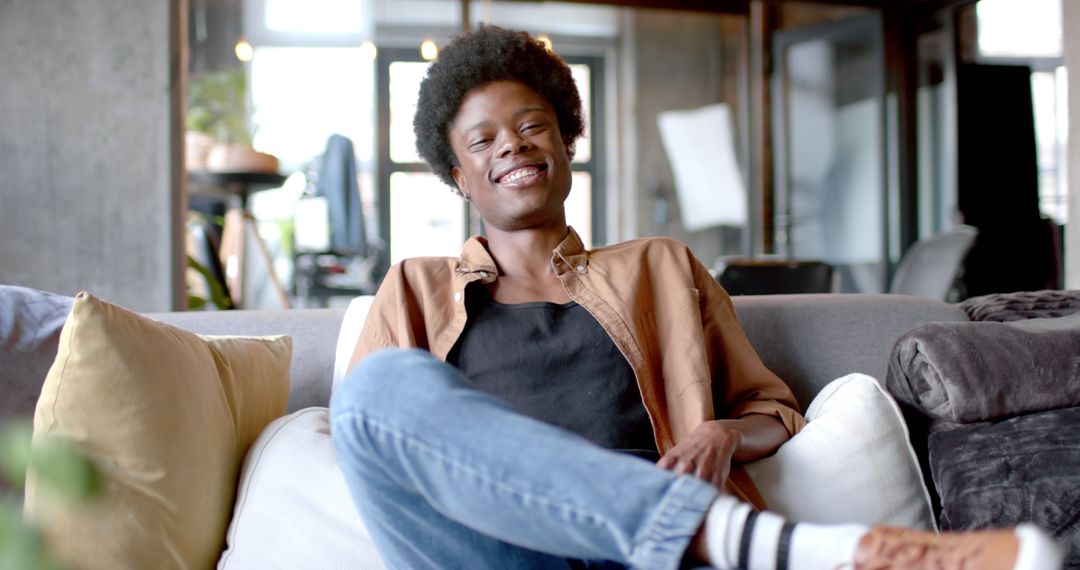 Cheerful Man with Afro Hairstyle Relaxing on Home Sofa - Free Images, Stock Photos and Pictures on Pikwizard.com