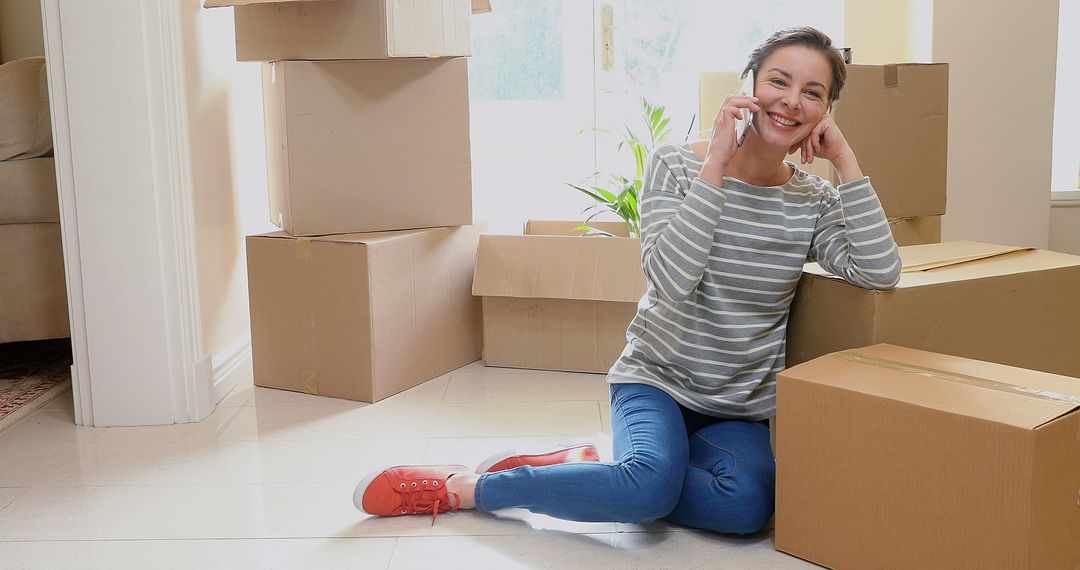 Happy Woman Sitting Among Moving Boxes While Talking on Phone - Free Images, Stock Photos and Pictures on Pikwizard.com