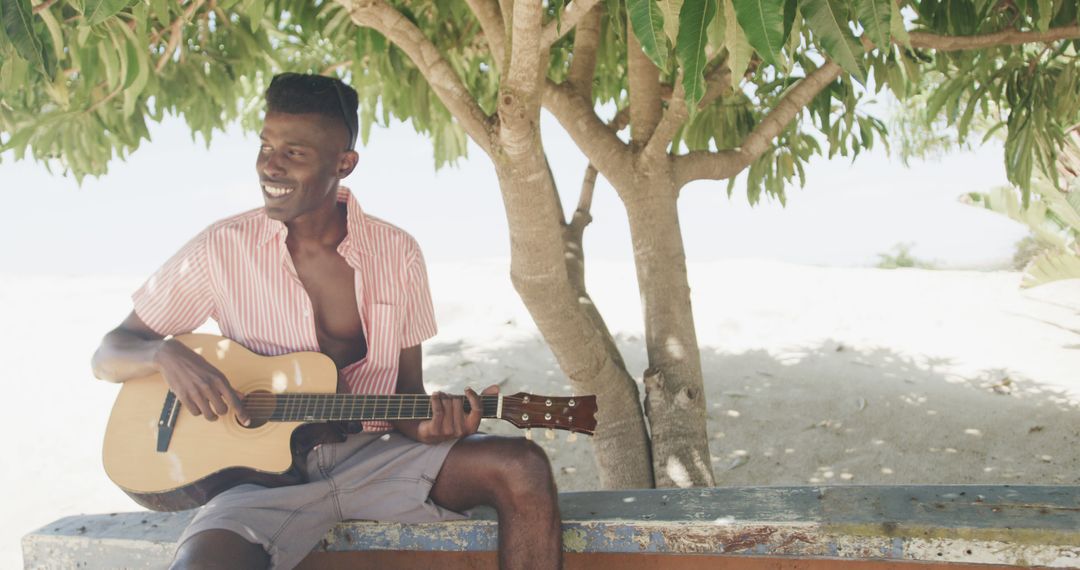 Young Man Playing Guitar Under Tree in Beach Setting - Free Images, Stock Photos and Pictures on Pikwizard.com