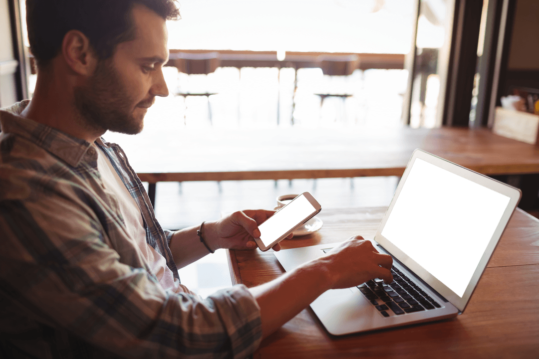 Young Man in Cafe Using Laptop and Mobile Phone with Transparent Screens