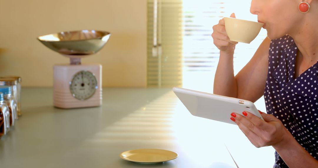 Woman Drinking Coffee While Using Tablet in Sunny Kitchen - Free Images, Stock Photos and Pictures on Pikwizard.com