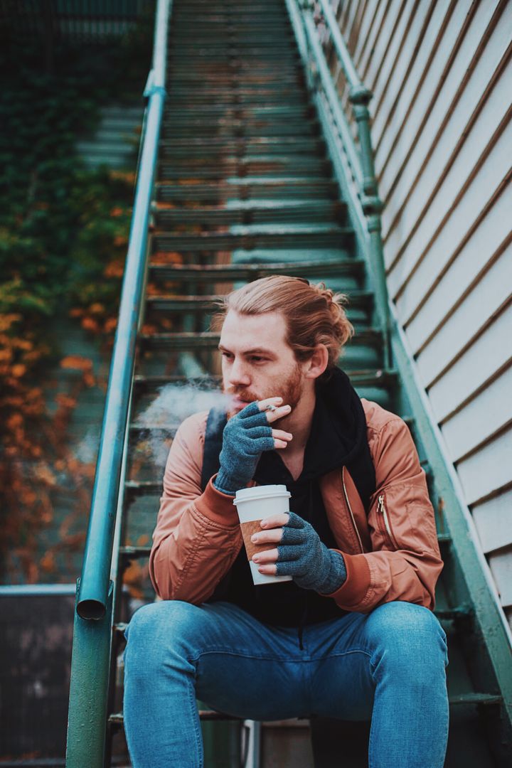 Young Man Smoking on Outdoor Stairway with Coffee - Free Images, Stock Photos and Pictures on Pikwizard.com