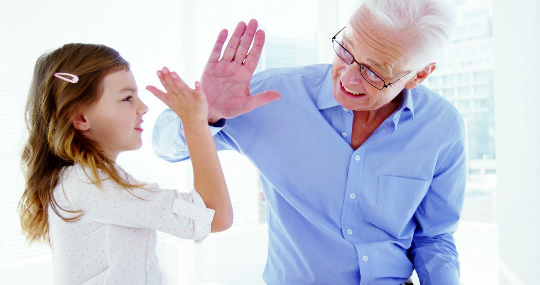 Happy Grandfather High-Fiving Granddaughter in Bright Room - Free Images, Stock Photos and Pictures on Pikwizard.com