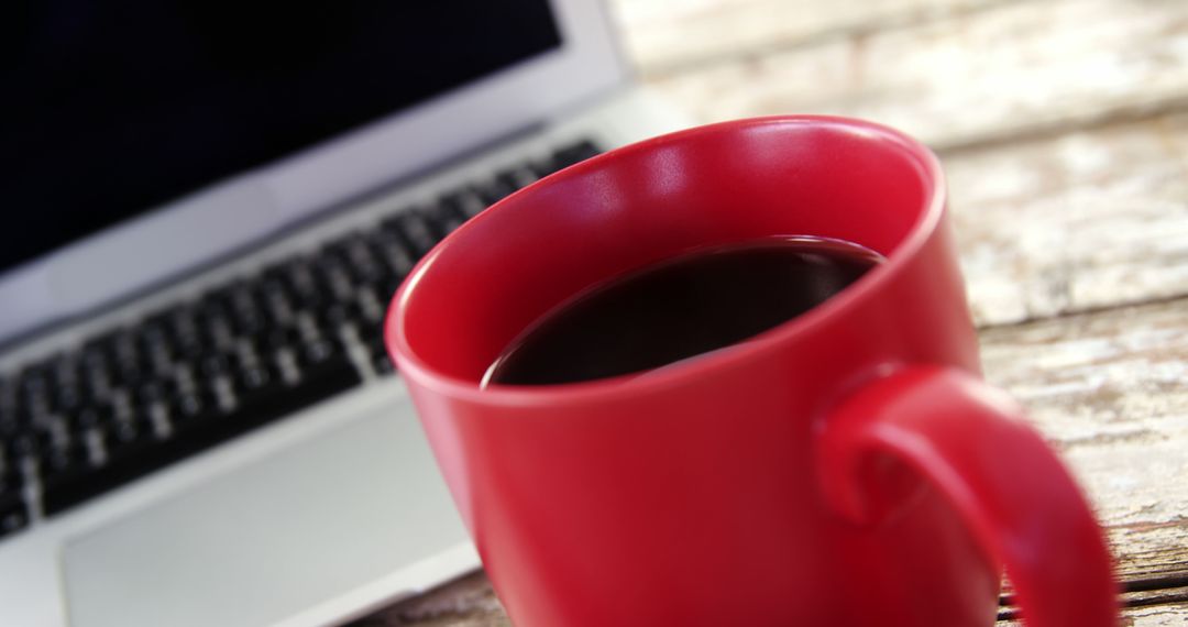 A red coffee mug sits in the foreground with a blurred laptop in the background, with copy space - Free Images, Stock Photos and Pictures on Pikwizard.com