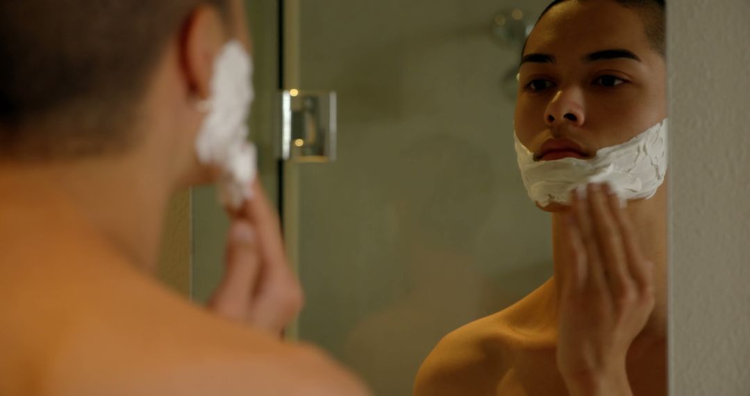 Young man applying shaving cream in front of mirror in bathroom - Free Images, Stock Photos and Pictures on Pikwizard.com