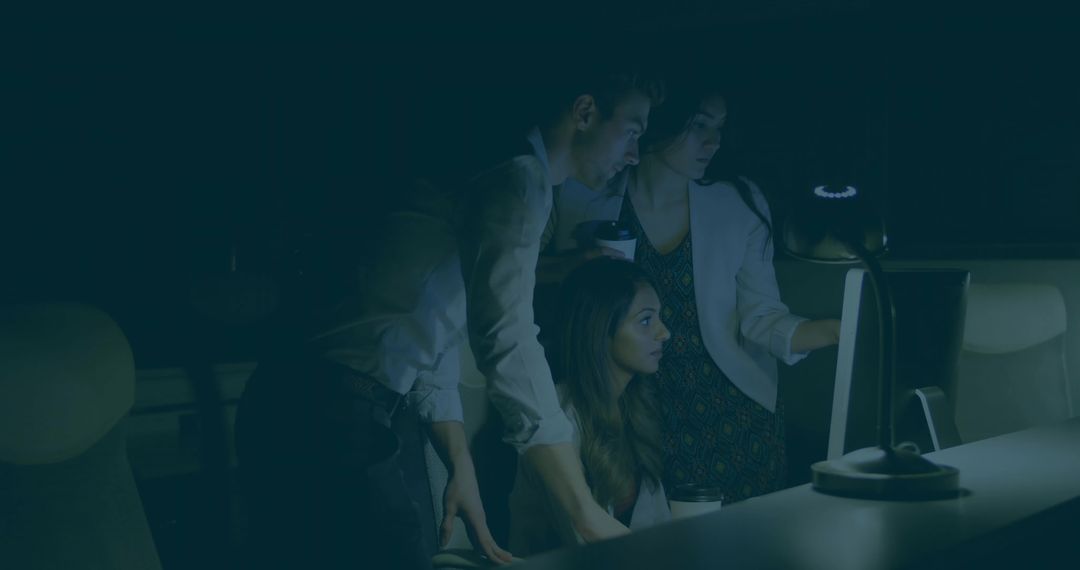Colleagues Collaborating Late Night Around Computer Screen Under Desk Lamp for Team Project