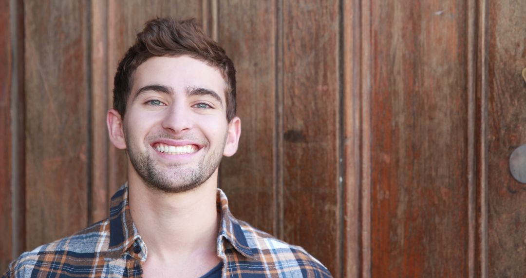 Smiling Young Man Wearing Plaid Shirt Against Wooden Background - Free Images, Stock Photos and Pictures on Pikwizard.com