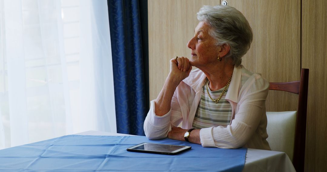 Thoughtful Elderly Woman Sitting by Window with Tablet - Free Images, Stock Photos and Pictures on Pikwizard.com