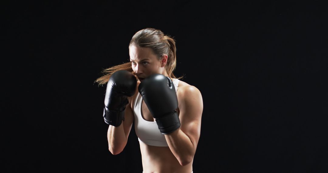 Focused Female Boxer Practicing Stance in Dark Gym