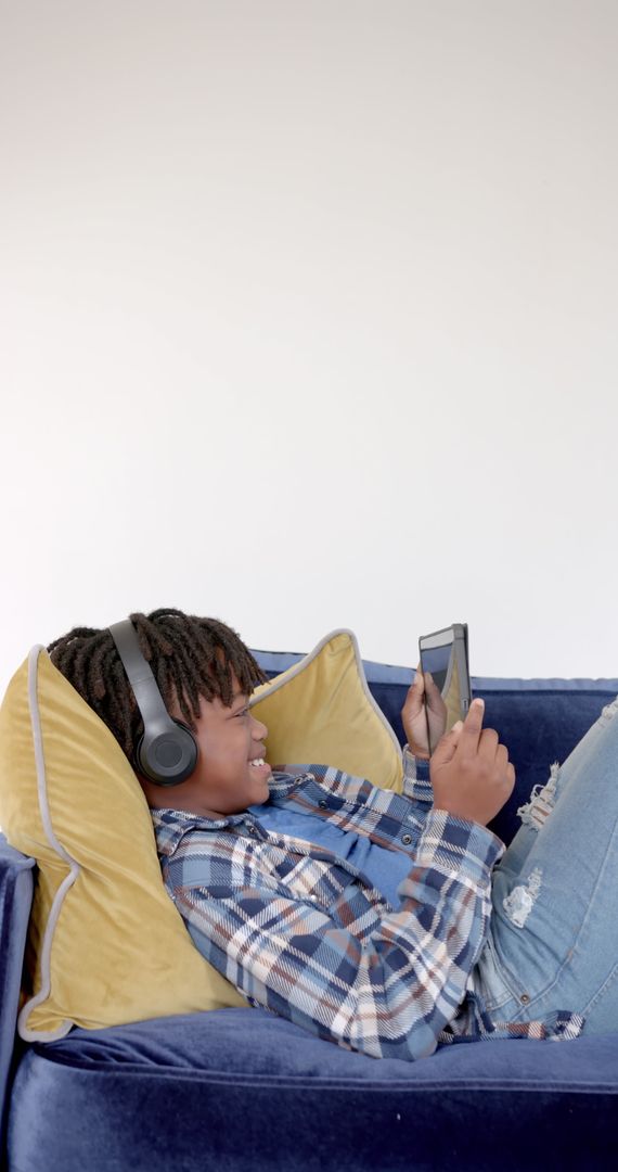 Smiling Boy Relaxing on Blue Sofa with Smartphone and Headphones