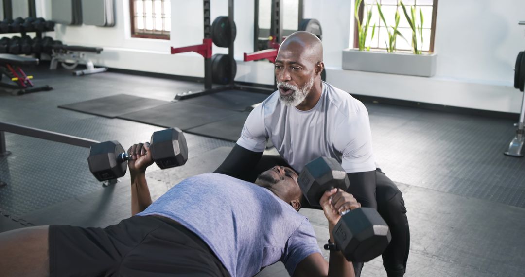 Senior Trainer Guiding Client in Dumbbell Bench Press at Modern Gym