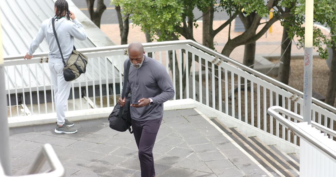Senior African American man walking up urban stairs checking smartphone while younger man talking