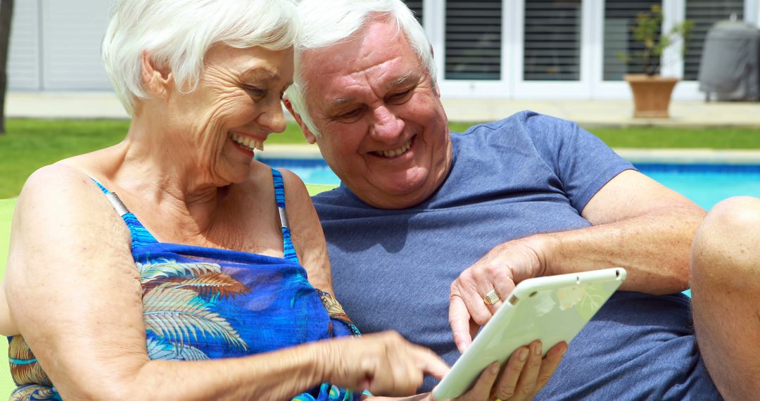 Senior Couple Enjoying Digital Tablet by Poolside