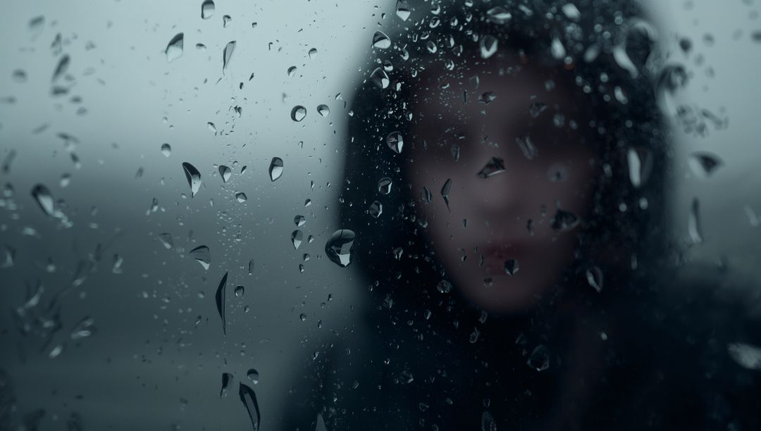 Moody Woman Behind Raindrop-Covered Glass in Urban Reflection
