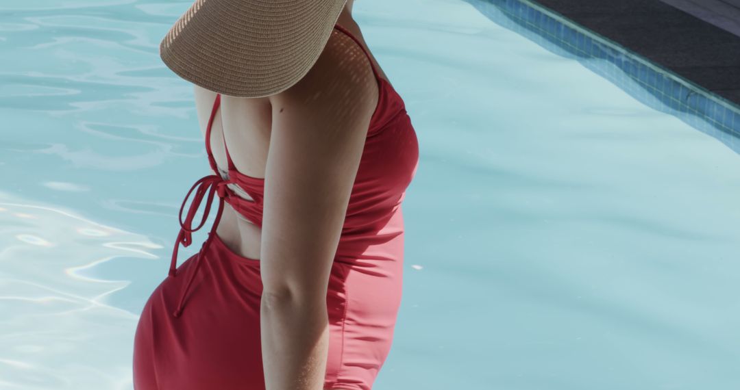 Woman wearing red swimsuit relaxing by pool in sun hat - Free Images, Stock Photos and Pictures on Pikwizard.com