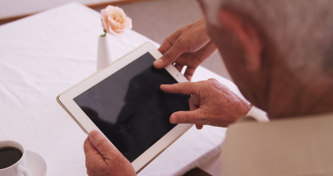 Senior Using Tablet At White Table With Coffee Cup And Flower - Free Images, Stock Photos and Pictures on Pikwizard.com