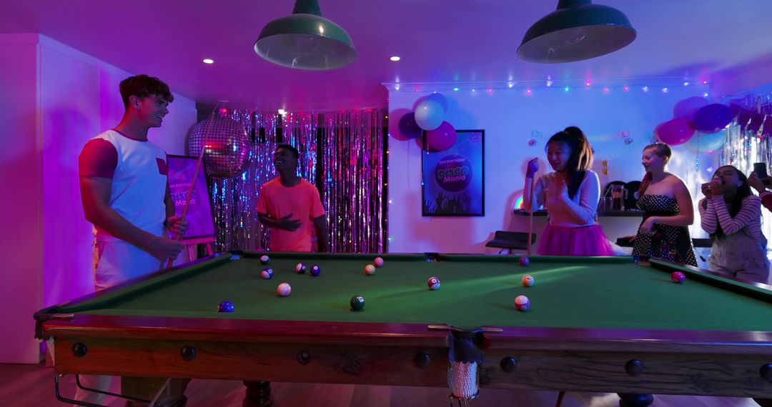 Diverse friends playing pool at neon-lit party room with disco ball and colorful lights