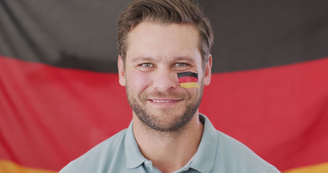 Confident man with German flag face paint smiling in front of German flag - Free Images, Stock Photos and Pictures on Pikwizard.com