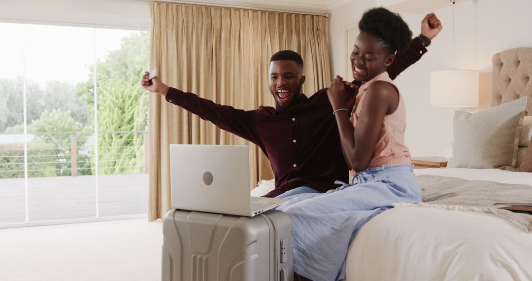 Excited Couple Using Laptop on Suitcase in Modern Bedroom