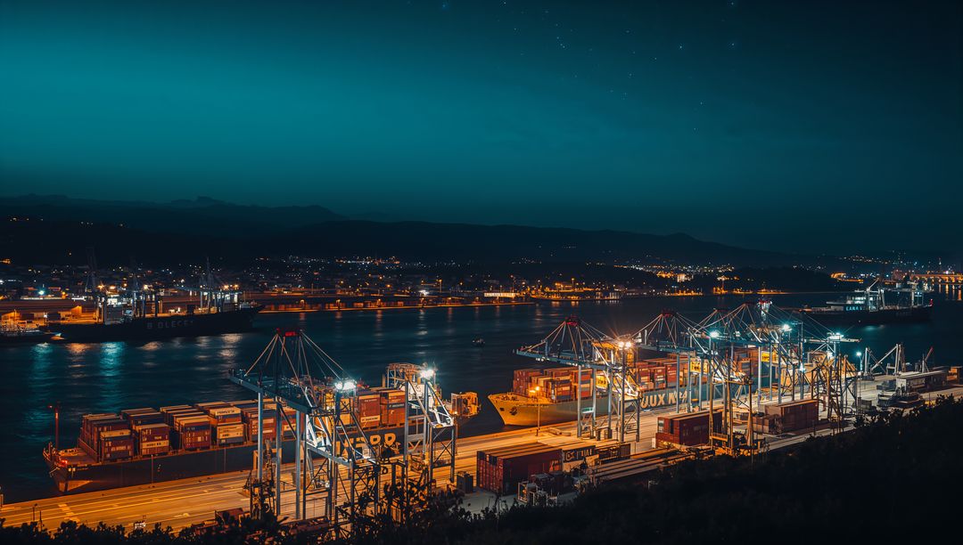 Gantry cranes illuminating container port and cargo ships along night waterfront