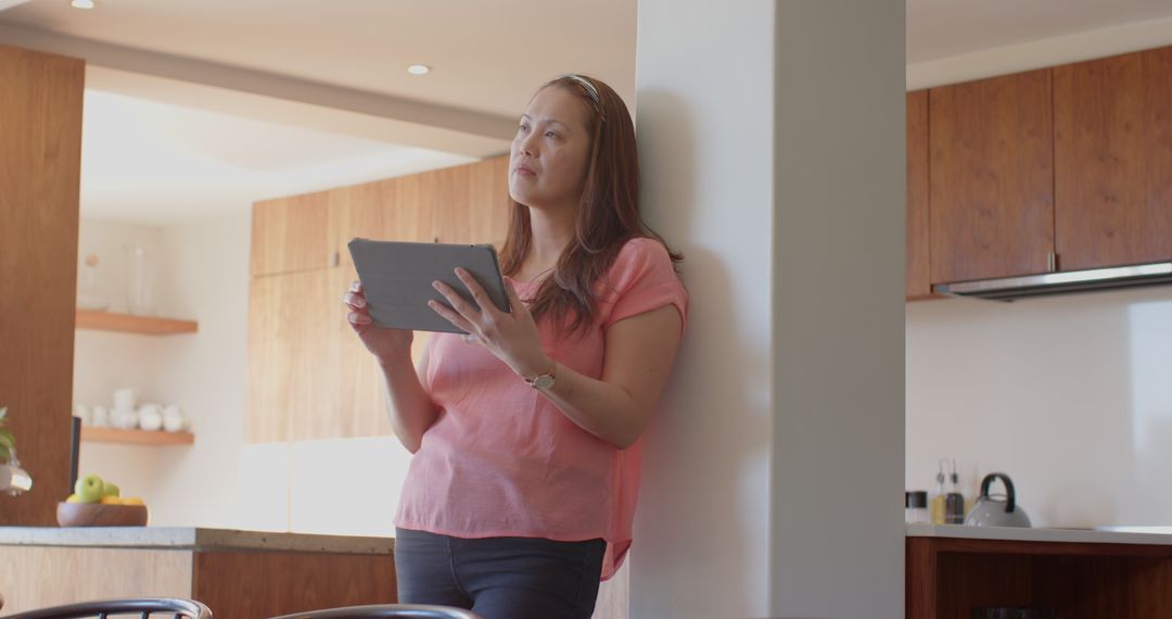 Contemplative Woman Using Tablet in Modern Kitchen