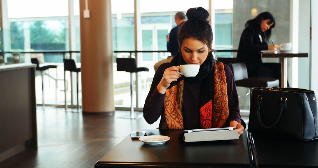 Young Woman Drinking Coffee and Using Tablet in Café - Free Images, Stock Photos and Pictures on Pikwizard.com