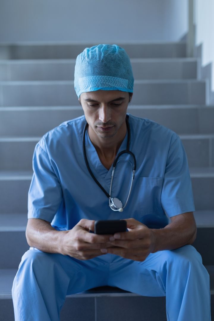 Male surgeon using mobile phone while sitting on staircase - Free Images, Stock Photos and Pictures on Pikwizard.com
