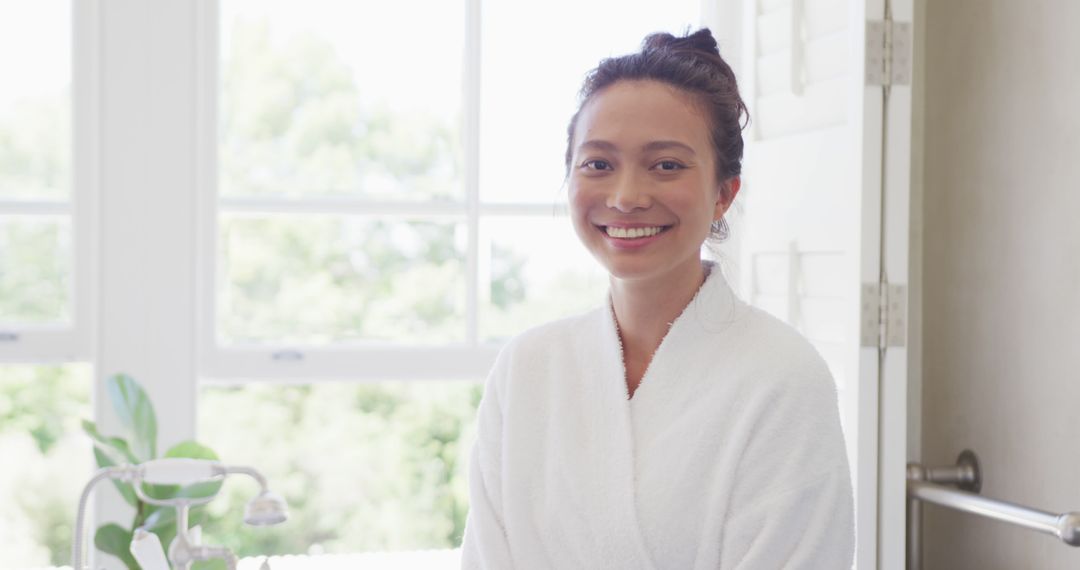 Smiling Woman in White Robe Relaxing by Window in Bright Room - Free Images, Stock Photos and Pictures on Pikwizard.com