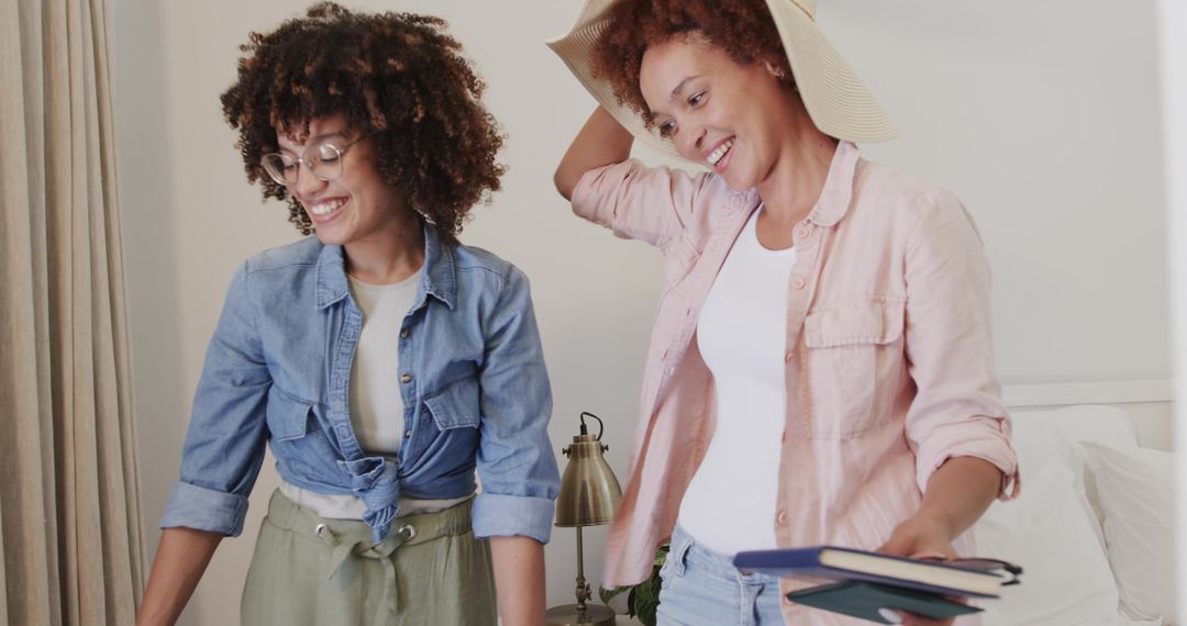 African American friends packing planners and smiling in sunlit casual bedroom