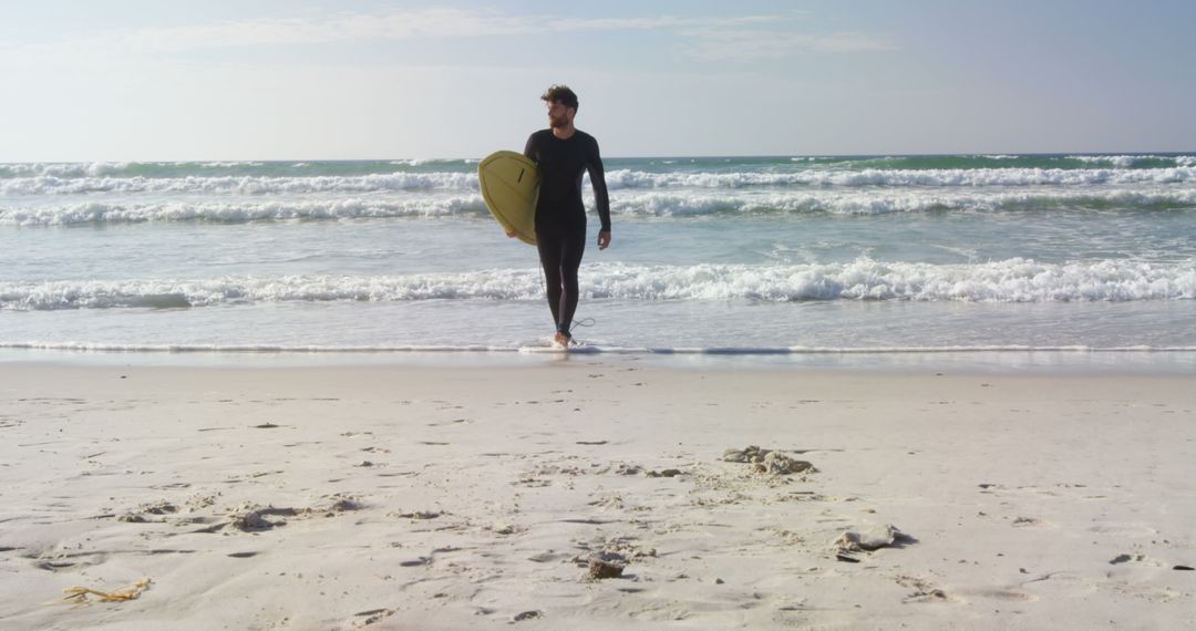 A young Caucasian man walks along the shore holding a surfboard, with copy space - Free Images, Stock Photos and Pictures on Pikwizard.com