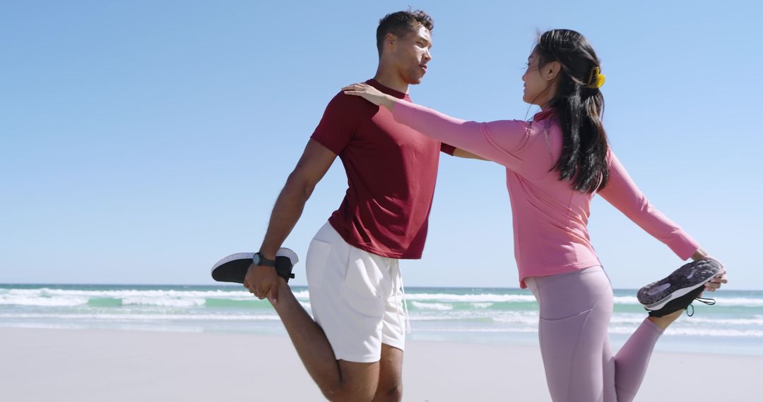 Couple Performing Partner Stretch on Sunny Beach Holding Sneakers While Balancing