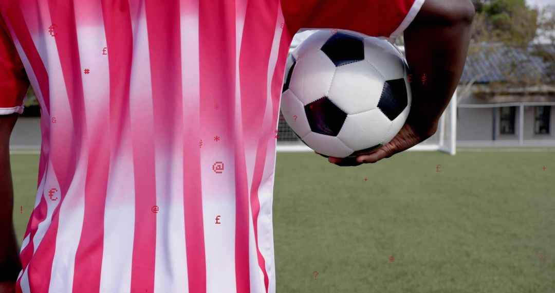 Cradling Soccer Player Holding Ball in Red-and-White Striped Jersey Facing Goal on Turf