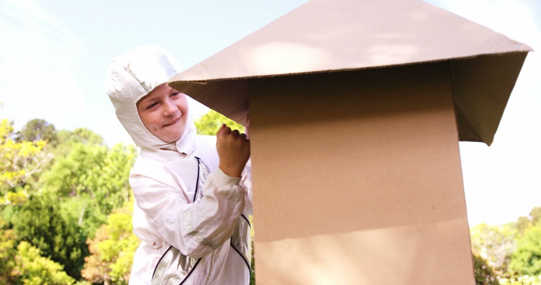 Child in Astronaut Costume Playing with Cardboard Spaceship Outdoors
