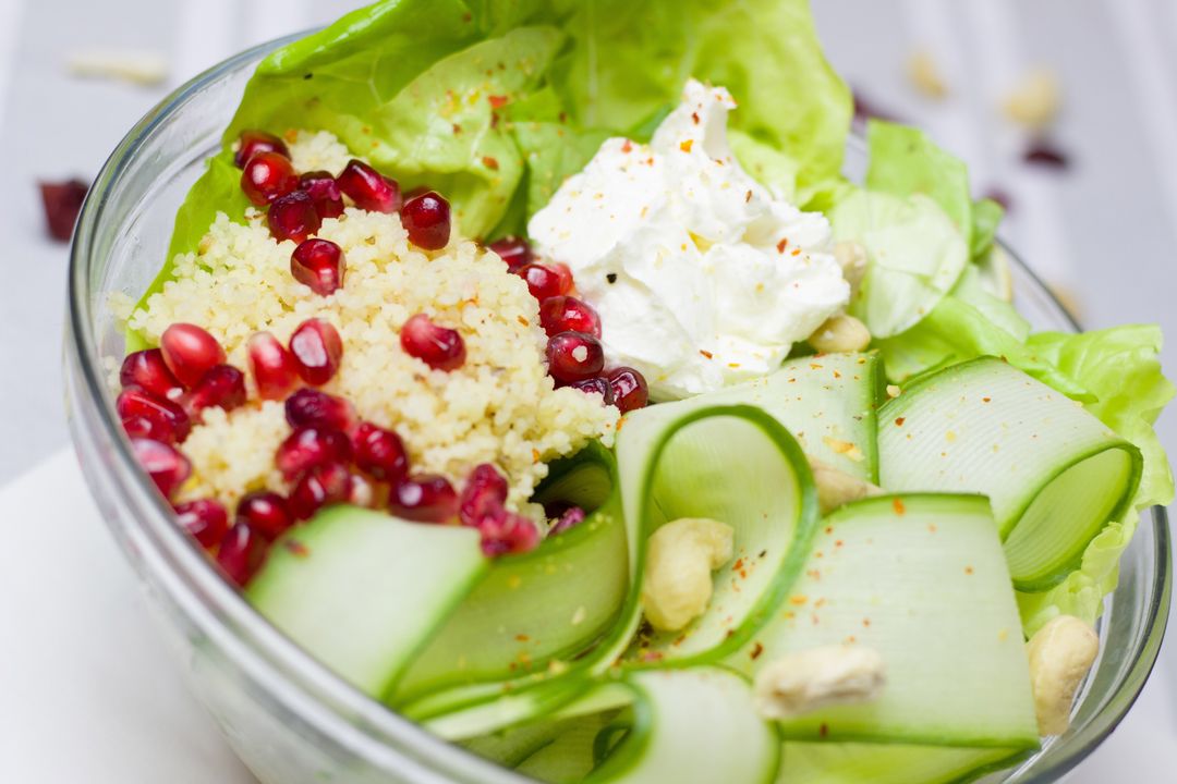Serving colorful couscous and pomegranate salad with zucchini ribbons and ricotta