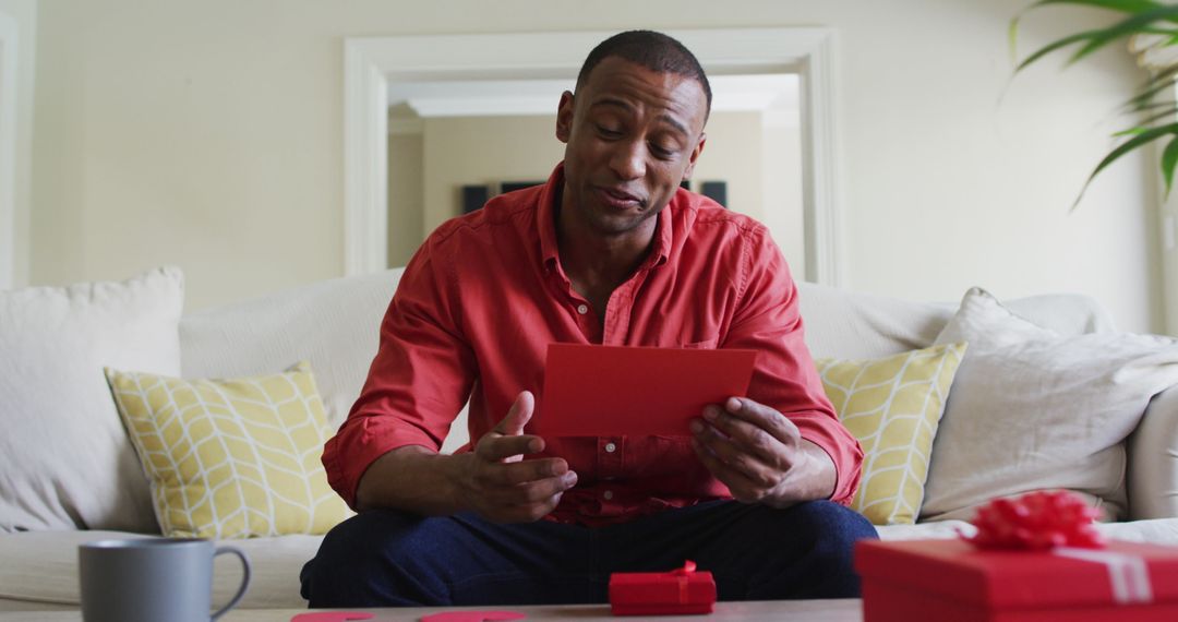 Joyful Man Reading Valentine’s Card on Sofa with Gifts Around
